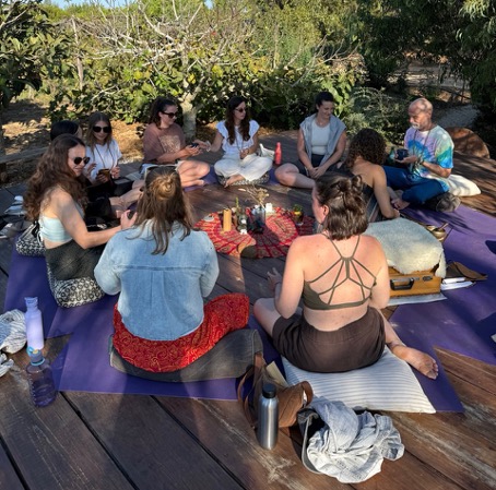 Gruppe von Yogis die gemeinsam im Kreis in der Natur sitzen und sich gegenseitig unterstützen